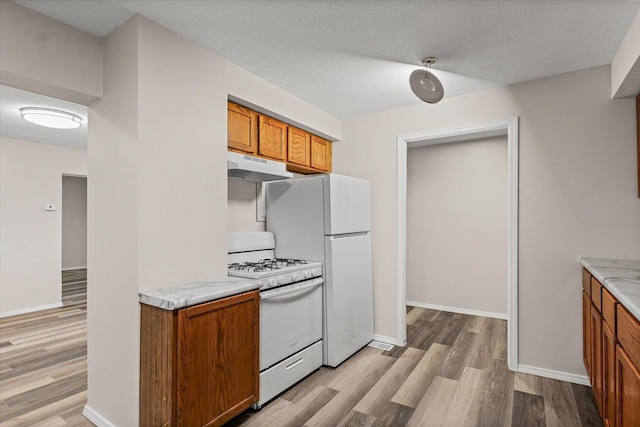 1010 N Neil St, Champaign, IL 61820 - kitchen with white gas range oven, under cabinet range hood, brown cabinetry, light wood-style floors, and a textured ceiling