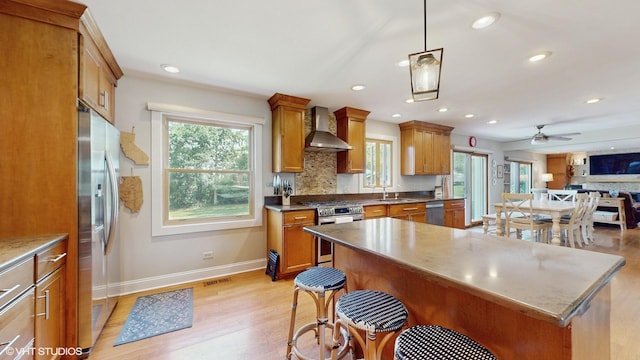 27W558 Ridgeview St, West Chicago, IL 60185 - kitchen featuring appliances with stainless steel finishes, wall chimney range hood, brown cabinets, open floor plan, and light wood-style flooring