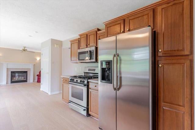 3310 Stonebridge Dr, Bloomington, IL 61704 - kitchen with stainless steel appliances, light wood-style flooring, brown cabinets, a ceiling fan, and a glass covered fireplace