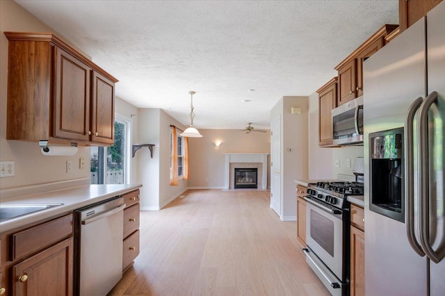 3310 Stonebridge Dr, Bloomington, IL 61704 - kitchen with appliances with stainless steel finishes, light wood-style flooring, a glass covered fireplace, a textured ceiling, and brown cabinetry
