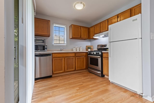 557 E Shag Bark Ln Unit H, Streamwood, IL 60107 - kitchen with stainless steel appliances, under cabinet range hood, light countertops, light wood-type flooring, and brown cabinetry