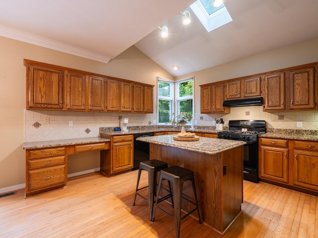 15955 Raintree Rd, Bloomington, IL 61705 - kitchen featuring black appliances, a skylight, brown cabinetry, light wood-style floors, and a breakfast bar