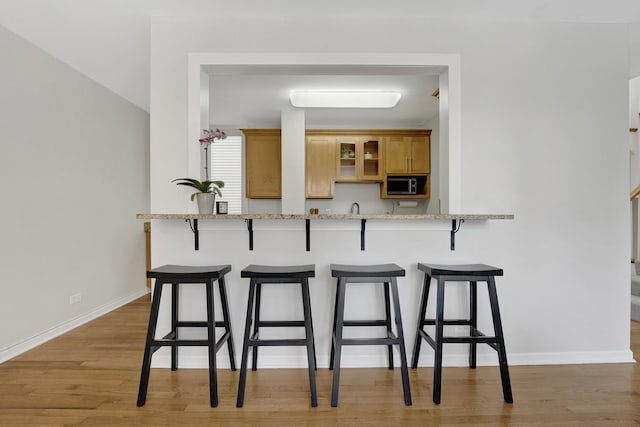 1315 W Webster Ave, Chicago, IL 60614 - kitchen featuring stainless steel microwave, a kitchen breakfast bar, light wood-style floors, light stone counters, and glass insert cabinets