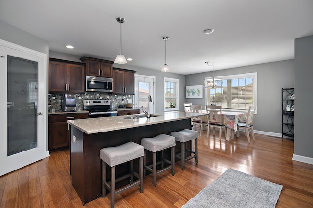 2225 Prairie Chase Dr, Bourbonnais, IL 60914 - kitchen featuring stainless steel appliances, dark brown cabinetry, a breakfast bar, decorative backsplash, and wood finished floors