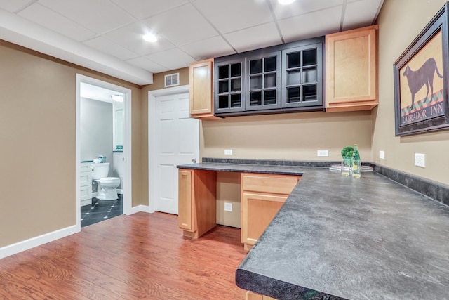 330 Dorchester Ln, Grayslake, IL 60030 - kitchen featuring dark countertops, light brown cabinets, a drop ceiling, glass insert cabinets, and light wood-style flooring