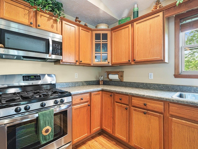 1375 Coven Cir, Davis, IL 61019 - kitchen with stainless steel appliances, light wood-type flooring, glass insert cabinets, a textured ceiling, and brown cabinets