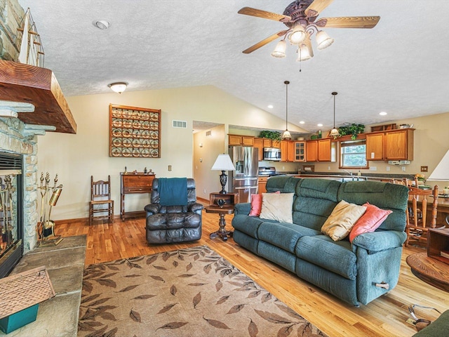 1375 Coven Cir, Davis, IL 61019 - living room with light wood-style flooring, vaulted ceiling, a stone fireplace, a ceiling fan, and a textured ceiling