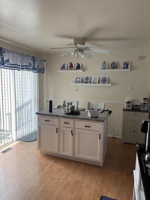kitchen with ceiling fan, light wood finished floors, white cabinetry, and a kitchen island