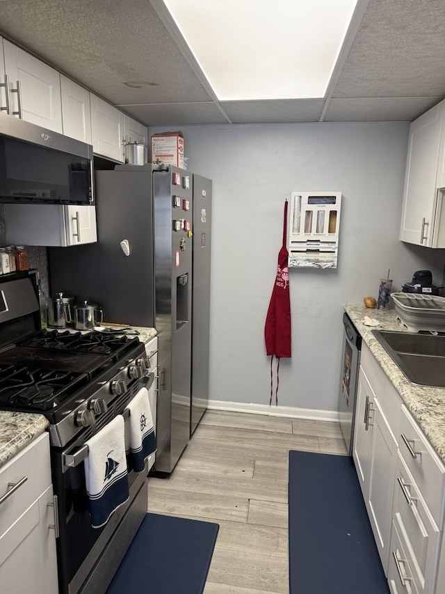 kitchen featuring stainless steel appliances, light wood-style floors, white cabinetry, and light stone countertops