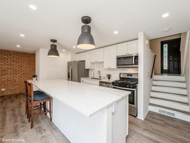 534 E Main St, Barrington, IL 60010 - kitchen featuring appliances with stainless steel finishes, brick wall, white cabinetry, light wood-style floors, and light stone counters