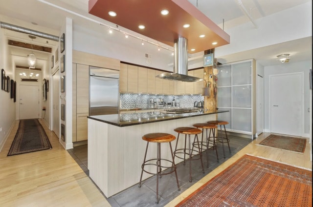 215 W Illinois St Unit 4C, Chicago, IL 60654 - kitchen featuring light wood-type flooring, dark countertops, tasteful backsplash, a breakfast bar area, and island range hood