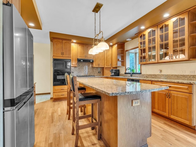 231 Deer Ln, Sleepy Hollow, IL 60118 - kitchen featuring black appliances, under cabinet range hood, light wood-style floors, a kitchen island, and light stone counters
