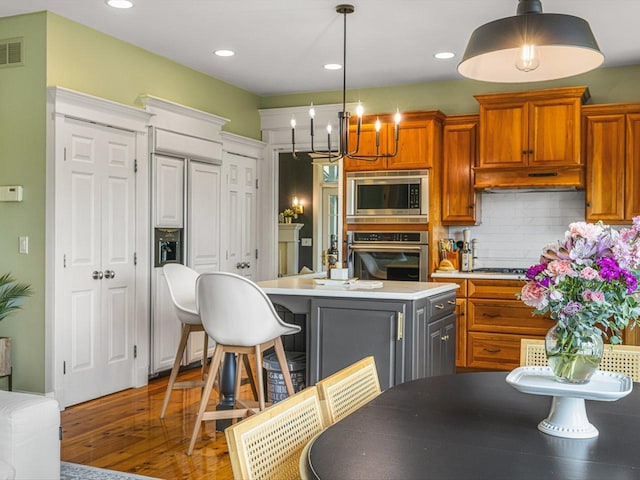 2207 N Elmkirk Pkwy N, Mchenry, IL 60051 - kitchen featuring built in appliances, a chandelier, wood finished floors, light countertops, and backsplash