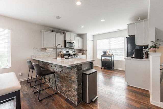 2366 Aurora Dr, Pingree Grove, IL 60140 - kitchen featuring appliances with stainless steel finishes, a peninsula, backsplash, a kitchen bar, and dark wood-type flooring