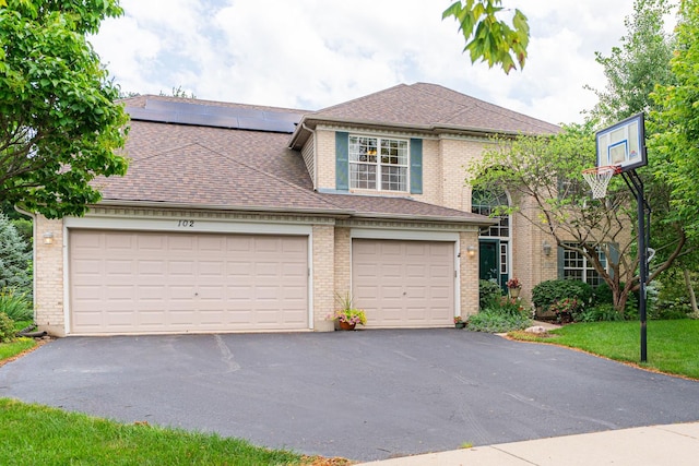 102 Quinlan Ave, Dekalb, IL 60115 - traditional-style house featuring driveway, brick siding, solar panels, a shingled roof, and an attached garage