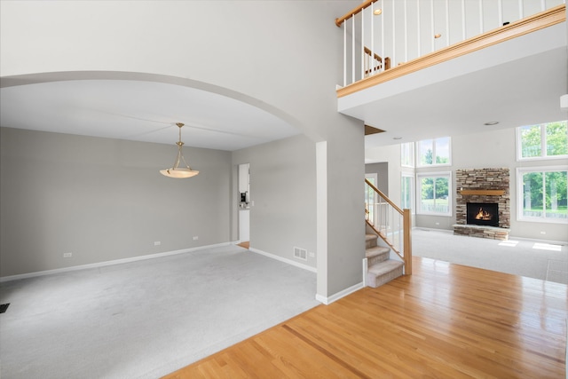 401 Kerry Ct, Prospect Heights, IL 60070 - unfurnished living room featuring arched walkways, stairs, a stone fireplace, wood finished floors, and a towering ceiling