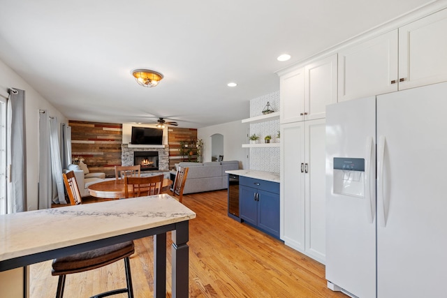 12351 W Warren Dr, Mokena, IL 60448 - kitchen with white fridge with ice dispenser, blue cabinets, a fireplace, a ceiling fan, and light wood-type flooring