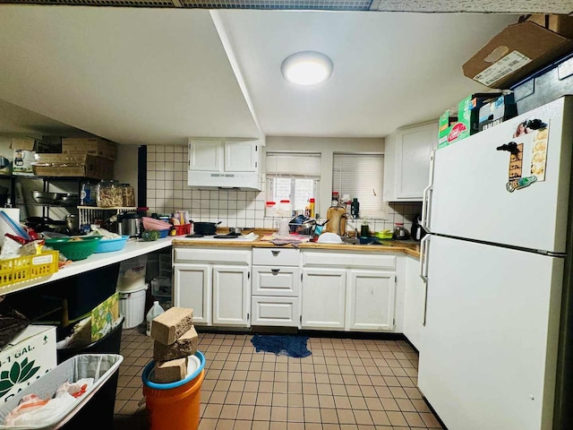 5221 W Montrose Ave, Chicago, IL 60641 - kitchen with freestanding refrigerator, white cabinetry, under cabinet range hood, tile patterned floors, and backsplash
