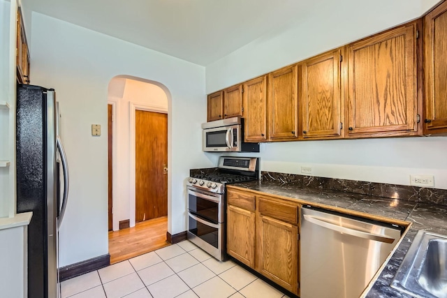4017 Park Ave, Brookfield, IL 60513 - kitchen featuring stainless steel appliances, arched walkways, light tile patterned floors, dark countertops, and brown cabinets