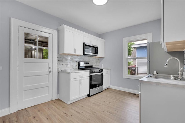 305 S Lewis Ave, Waukegan, IL 60085 - kitchen featuring appliances with stainless steel finishes, light wood-style floors, light countertops, backsplash, and white cabinetry