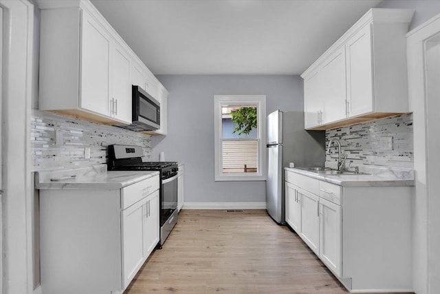 305 S Lewis Ave, Waukegan, IL 60085 - kitchen with appliances with stainless steel finishes, light countertops, decorative backsplash, light wood-style flooring, and white cabinetry