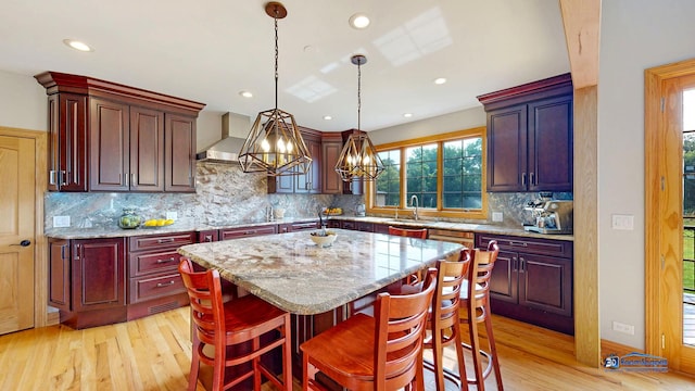 19113 Lauren Ln, Marengo, IL 60152 - kitchen with light wood-type flooring, wall chimney exhaust hood, a kitchen island, decorative light fixtures, and light stone counters