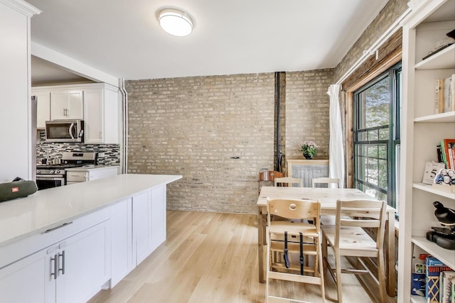 7021 N Sheridan Rd Unit 1, Chicago, IL 60626 - kitchen with appliances with stainless steel finishes, brick wall, white cabinets, light countertops, and light wood-style flooring
