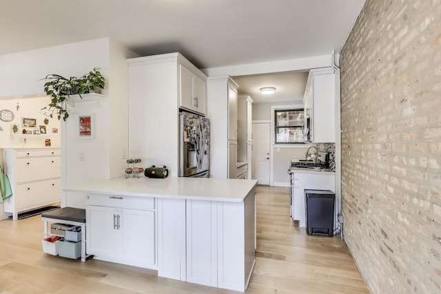 7021 N Sheridan Rd Unit 1, Chicago, IL 60626 - kitchen with appliances with stainless steel finishes, brick wall, white cabinetry, light wood finished floors, and light countertops