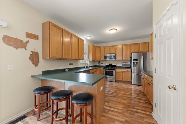 7425 Rosewind Dr, Plainfield, IL 60586 - kitchen featuring appliances with stainless steel finishes, a peninsula, a breakfast bar area, dark wood finished floors, and dark countertops