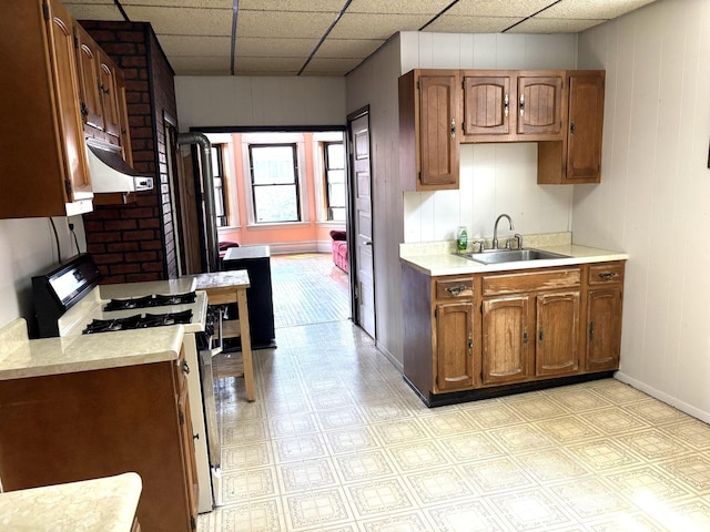 2838 S Keeley St, Chicago, IL 60608 - kitchen with range with gas stovetop, light countertops, under cabinet range hood, brown cabinetry, and a paneled ceiling