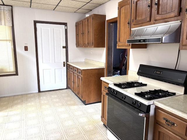 2838 S Keeley St, Chicago, IL 60608 - kitchen with white gas range oven, under cabinet range hood, light countertops, brown cabinetry, and a drop ceiling