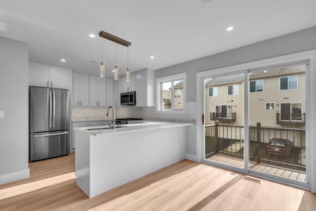 24642 George Washington Dr, Plainfield, IL 60544 - kitchen with appliances with stainless steel finishes, light countertops, light wood-style floors, a peninsula, and pendant lighting