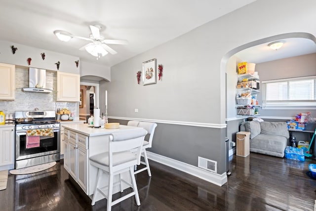 6921 26th St, Berwyn, IL 60402 - kitchen featuring stainless steel gas range oven, wall chimney range hood, arched walkways, a ceiling fan, and dark wood-style flooring
