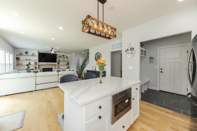 207 Eldon Dr, Downs, IL 61736 - kitchen featuring stainless steel microwave, a ceiling fan, a fireplace, a center island, and white cabinets