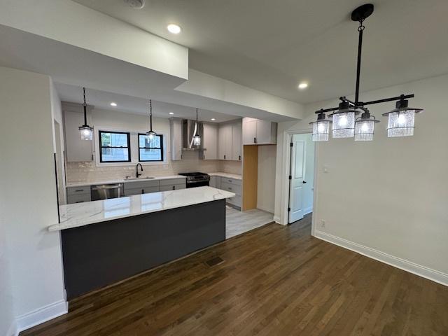 3512 Woodside Ave, Brookfield, IL 60513 - kitchen with wall chimney exhaust hood, a peninsula, black range oven, dark wood-style flooring, and light stone countertops