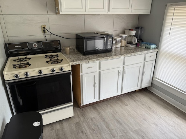 1250 Corbin St, Rockford, IL 61102 - kitchen featuring white gas range, black microwave, white cabinets, and light wood-type flooring