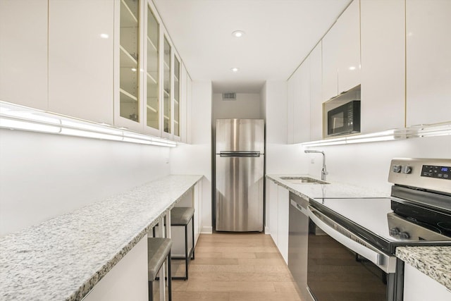 1550 N Lake Shore Dr Unit 2A, Chicago, IL 60610 - kitchen featuring stainless steel appliances, light wood finished floors, white cabinets, glass insert cabinets, and light stone counters