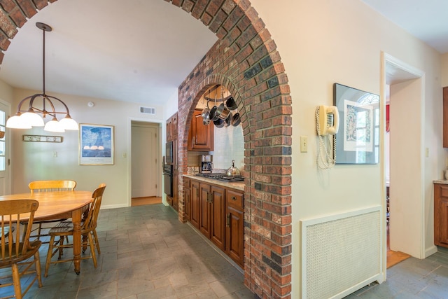 1286 W Stephenson St, Freeport, IL 61032 - kitchen with stone tile flooring, light countertops, stainless steel gas stovetop, brown cabinetry, and hanging light fixtures