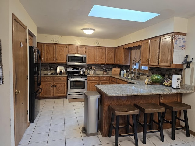 18510 Willow Ln, Lansing, IL 60438 - kitchen with stainless steel appliances, a peninsula, tasteful backsplash, a skylight, and brown cabinets