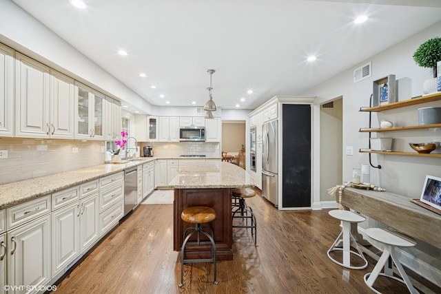 2113 Berwick St, Inverness, IL 60067 - kitchen featuring stainless steel appliances, a center island, a kitchen bar, wood finished floors, and glass insert cabinets
