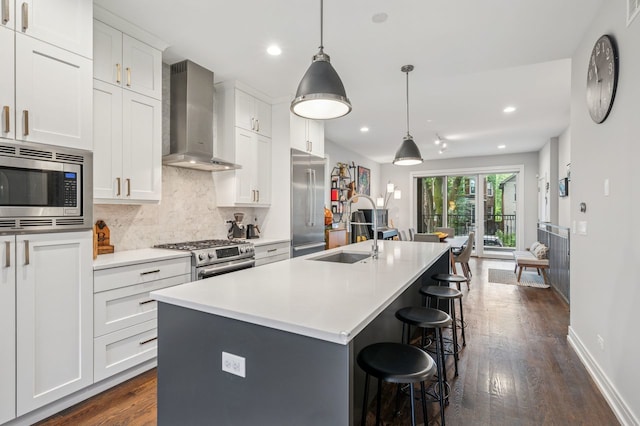 2422 W Lyndale St Unit 1E, Chicago, IL 60647 - kitchen featuring stainless steel appliances, wall chimney exhaust hood, dark wood-style floors, a kitchen island with sink, and a breakfast bar