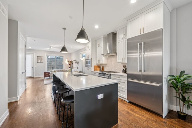 2422 W Lyndale St Unit 1E, Chicago, IL 60647 - kitchen with built in appliances, wall chimney range hood, a kitchen island with sink, white cabinets, and a breakfast bar area