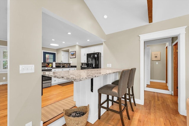 411 Hessel Blvd, Champaign, IL 61820 - kitchen with black refrigerator with ice dispenser, stainless steel range, white cabinets, lofted ceiling, and a kitchen bar