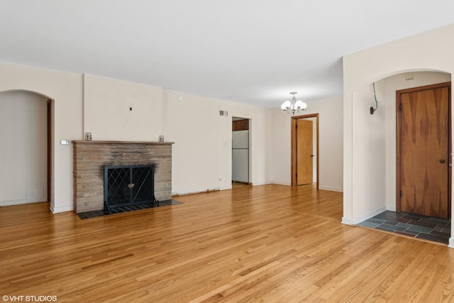 8024 W Charmaine Rd, Norridge, IL 60706 - unfurnished living room with light wood-style flooring, a chandelier, a stone fireplace, and arched walkways