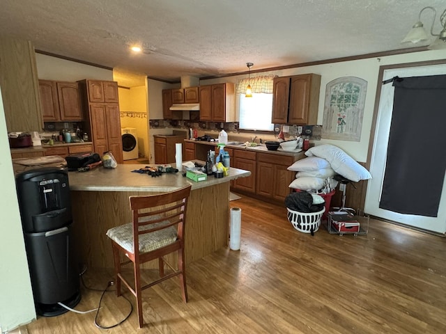 810 Harding Ave, Gillespie, IL 62033 - kitchen with washer / clothes dryer, a textured ceiling, under cabinet range hood, wood finished floors, and a kitchen breakfast bar