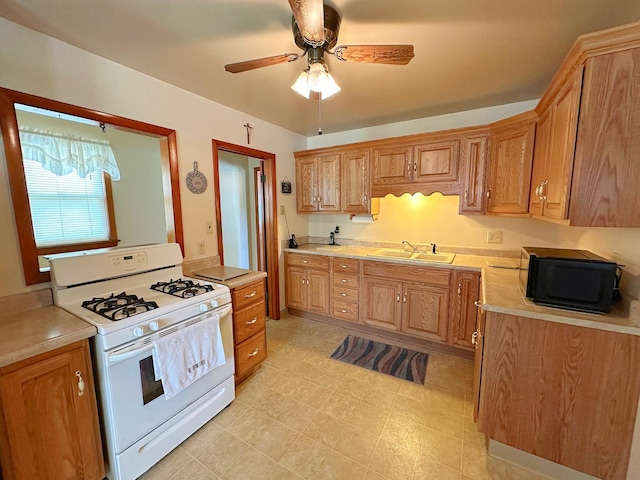 919 S Vermillion St, Streator, IL 61364 - kitchen featuring white range with gas cooktop, black microwave, light countertops, a ceiling fan, and brown cabinetry