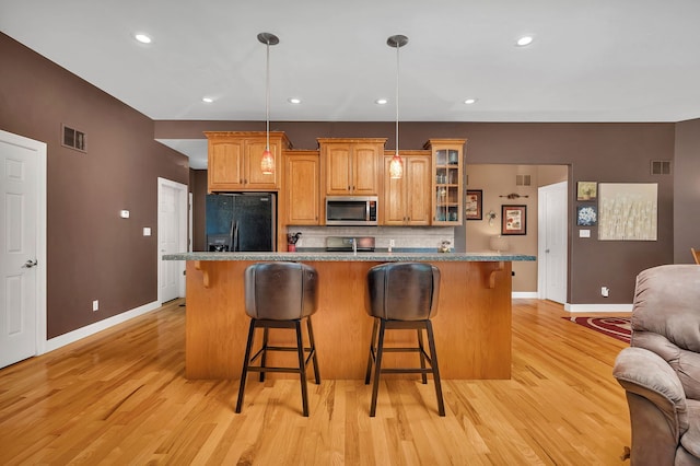 300 Village Ln, Seneca, IL 61360 - kitchen with black fridge, stainless steel microwave, a kitchen breakfast bar, backsplash, and light wood finished floors
