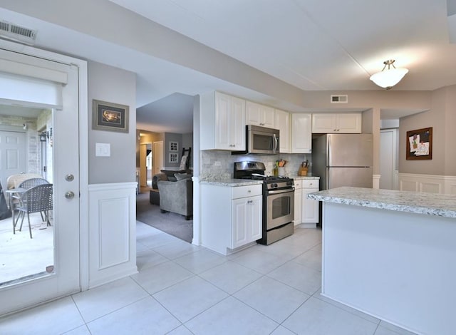 14031 Norwich Ln Unit 101, Orland Park, IL 60467 - kitchen featuring appliances with stainless steel finishes, white cabinets, wainscoting, light stone countertops, and a decorative wall