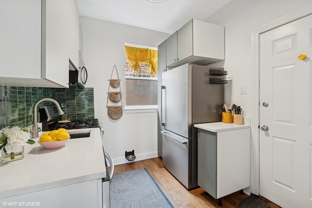 3555 W Lyndale St Unit 3B, Chicago, IL 60647 - kitchen featuring appliances with stainless steel finishes, light wood-type flooring, tasteful backsplash, light countertops, and white cabinets