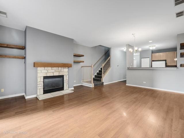 835 Genesee Dr, Naperville, IL 60563 - unfurnished living room with wood finished floors, a stone fireplace, stairs, and a chandelier